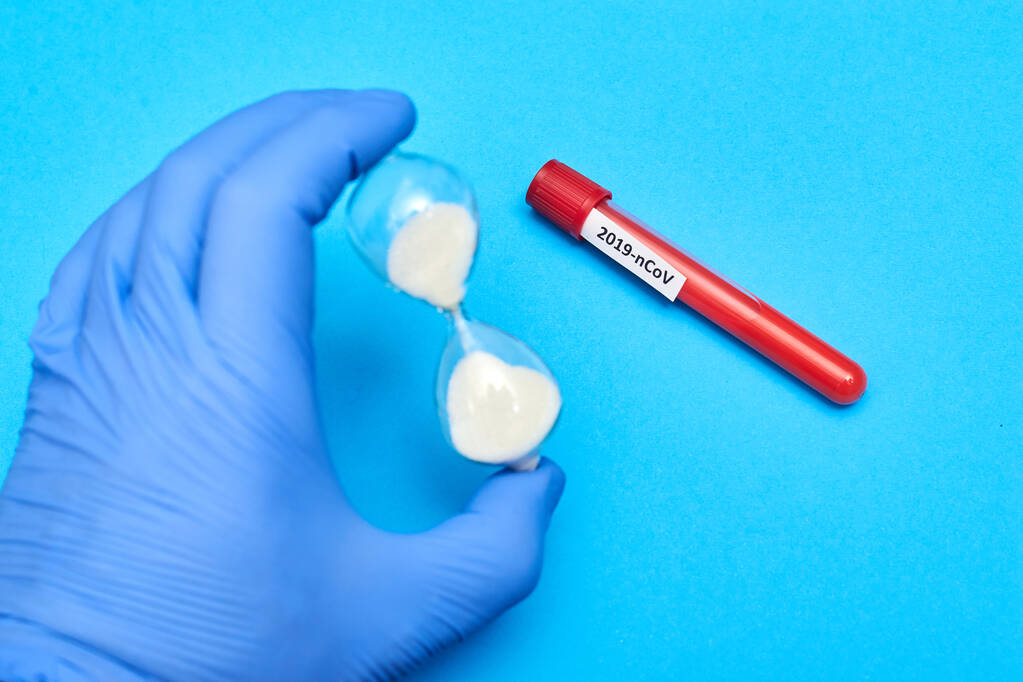 Coronavírus - inscrição em um tubo de teste com sangue na mão em uma luva de borracha em um fundo azul
. - Foto, Imagem