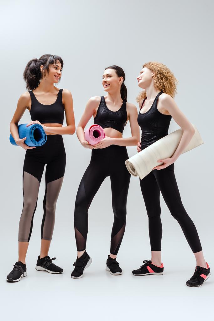 mulheres alegres e multiculturais segurando tapetes de fitness em branco
  - Foto, Imagem