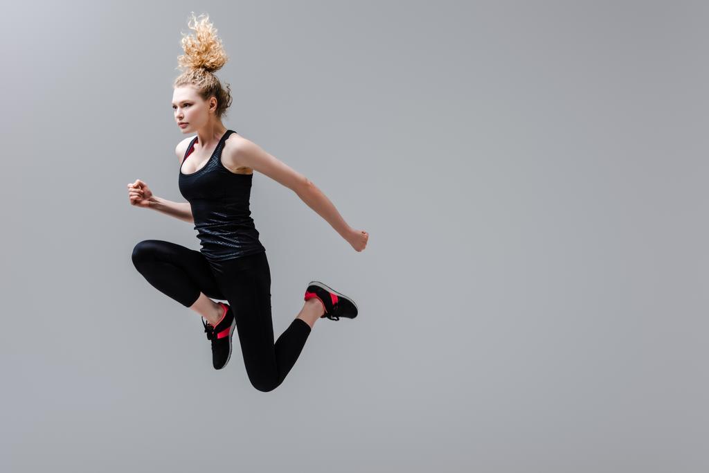 lockige Sportlerin in Sportkleidung springt vereinzelt auf grau  - Foto, Bild