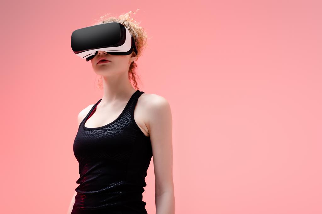 junge Frau in Sportbekleidung und Virtual-Reality-Headset auf rosa  - Foto, Bild