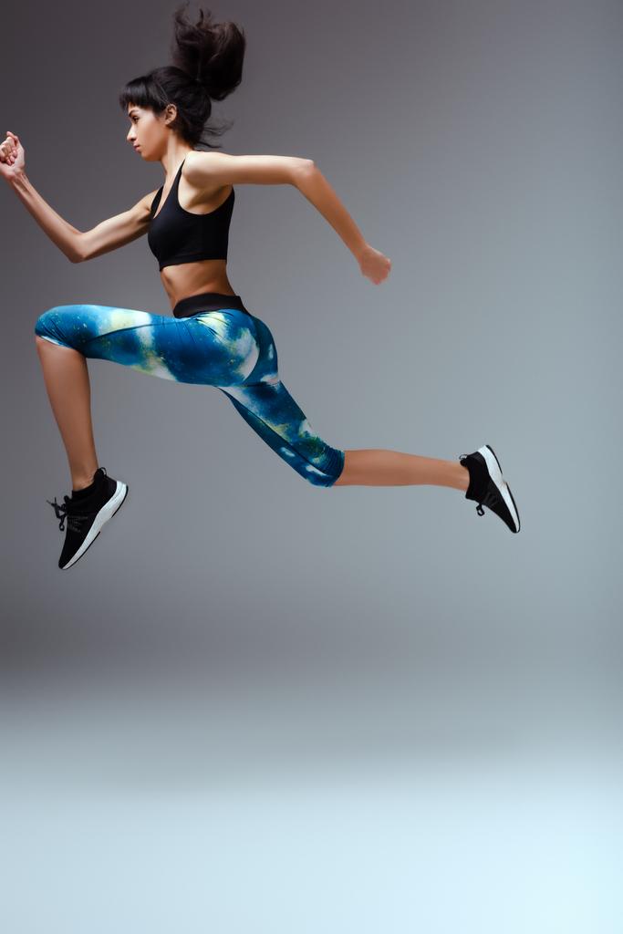Seitenansicht eines afrikanisch-amerikanischen Mädchens in Sportbekleidung, das auf grau springt  - Foto, Bild