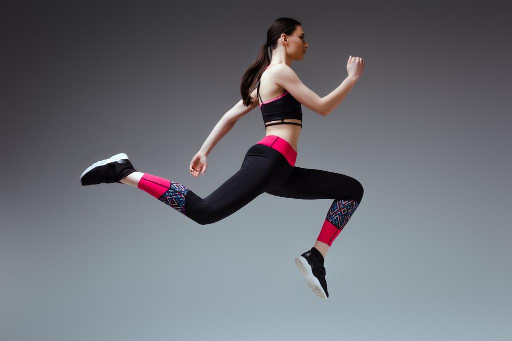 vista lateral da mulher bonita em sportswear pulando em cinza
 - Foto, Imagem