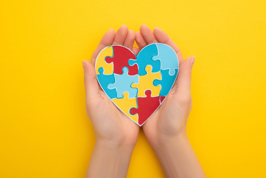 částečný pohled na ženu držící puzzle srdce na žluté - Fotografie, Obrázek
