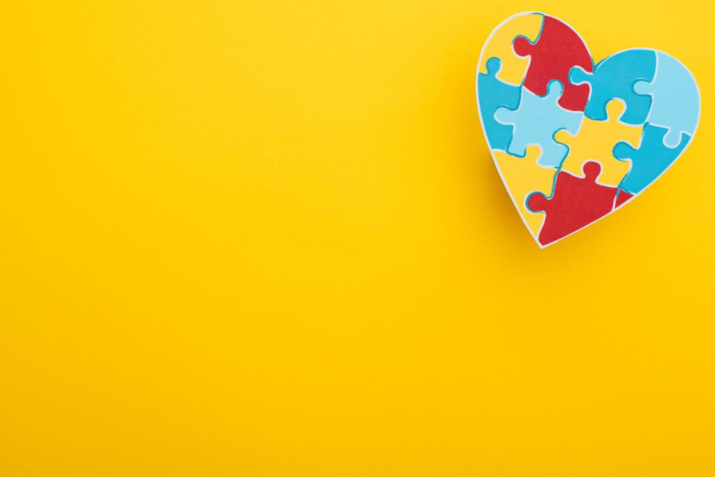 Draufsicht auf buntes Herz mit Puzzle auf gelb zum Welt-Autismus-Tag - Foto, Bild