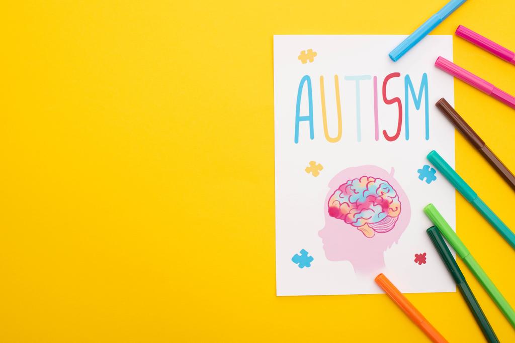 自閉症の文字と黄色に隔離された子供の絵が書かれた紙に書かれたフェルトペンの上からの眺め - 写真・画像