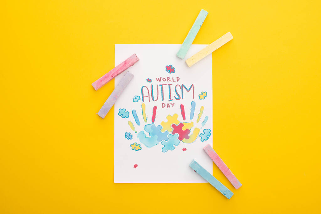 vista superior de la tarjeta con rompecabezas y las impresiones de mano para el Día Mundial del Autismo aislado en amarillo con tiza
 - Foto, Imagen