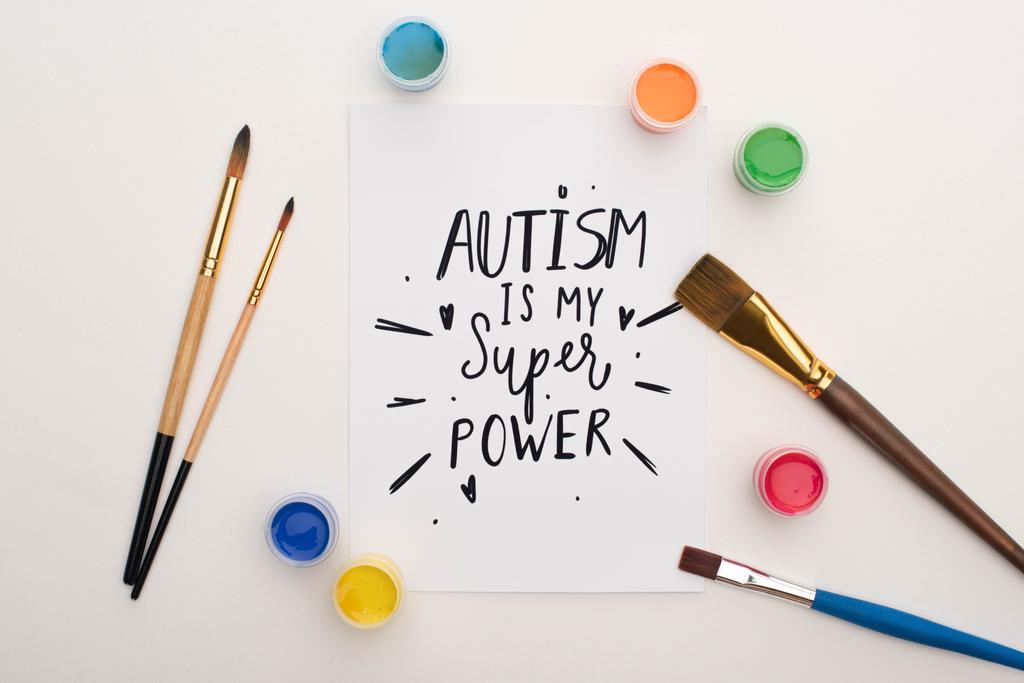 Draufsicht auf Farben, Pinsel und Karte mit Autismus ist mein Superpower-Schriftzug auf Weiß - Foto, Bild