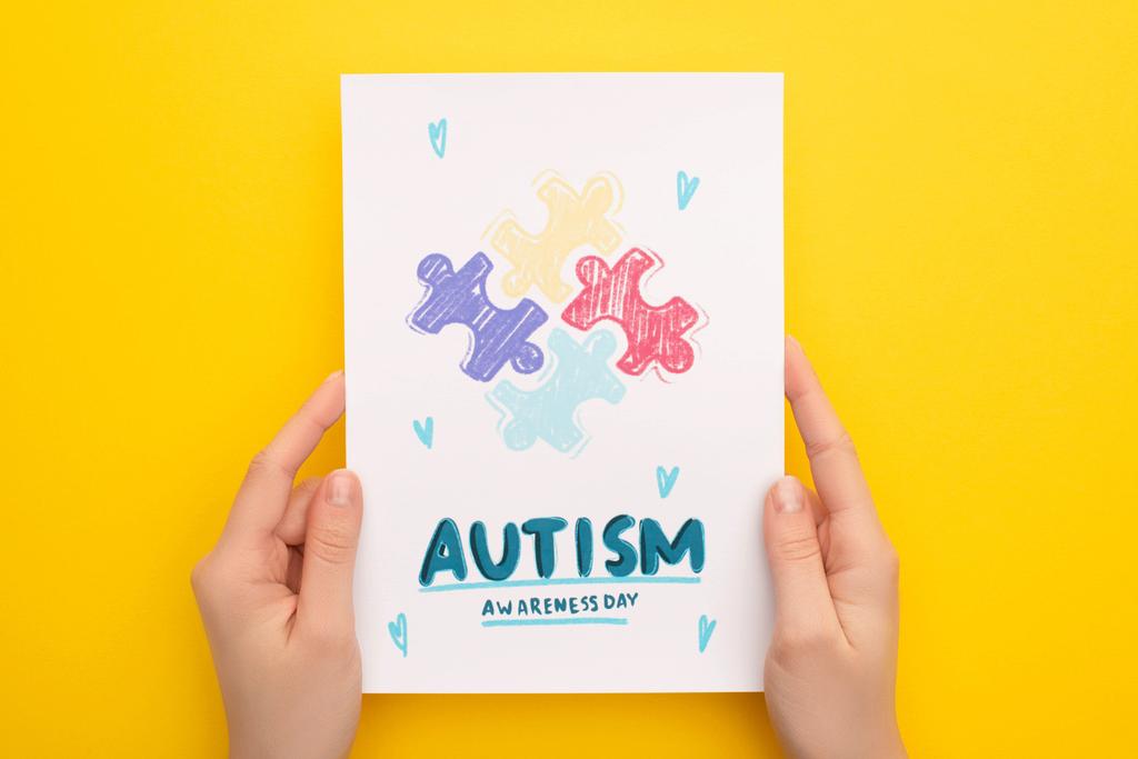 cropped view of woman holding card with puzzle for Autism Awareness Day on yellow - Photo, Image