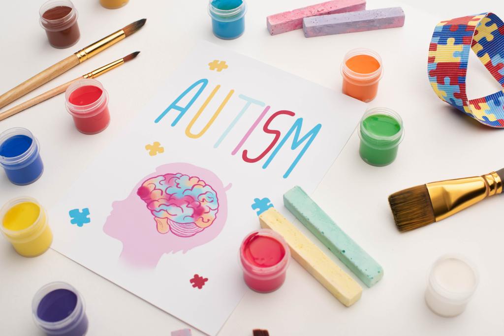 карточка со словом аутизма и рисунок головы с мозгом на белом с кисточками, мелом и красками
 - Фото, изображение