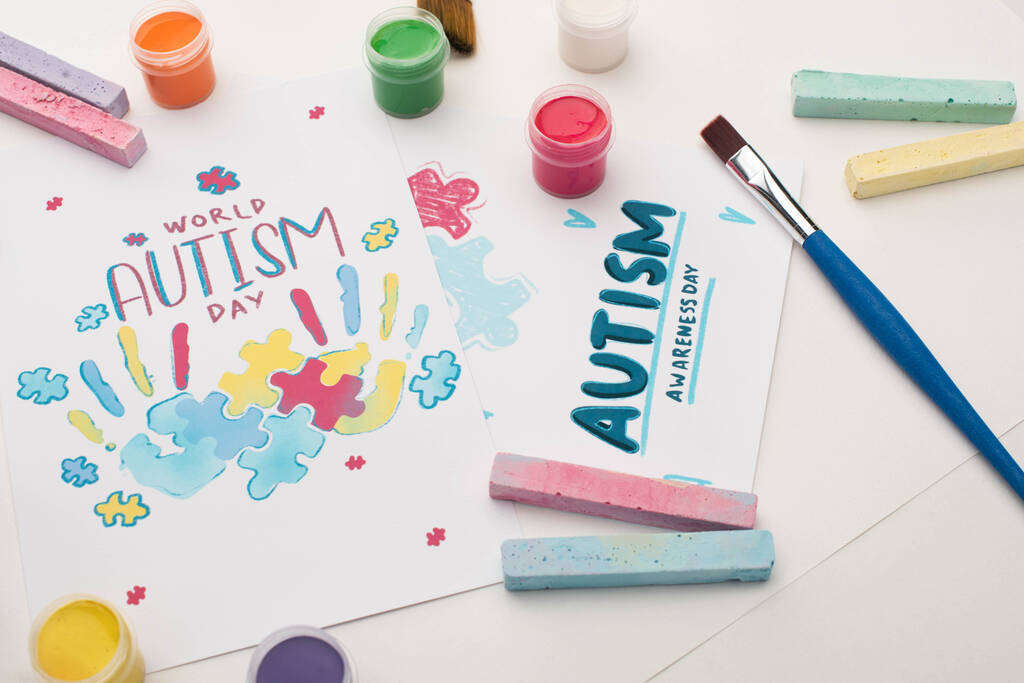 kaarten voor Wereld Autisme Dag belettering en schilderen van puzzel en handafdrukken op wit met verf borstels, krijt en verf - Foto, afbeelding