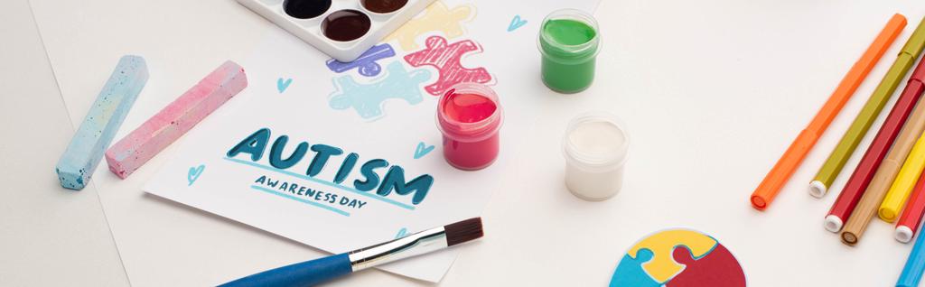 plano panorámico de la tarjeta con Autism Awareness Day letras y pintura de rompecabezas en blanco con pinceles, tiza y marcadores
 - Foto, imagen