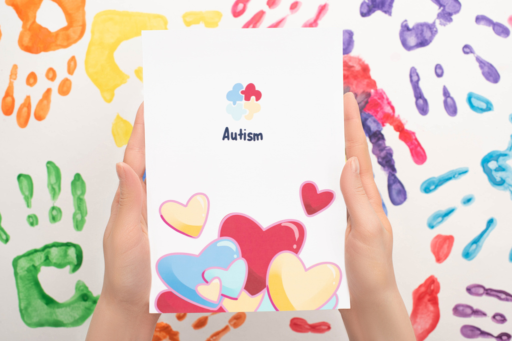 cropped view of woman holding card with Autism word and hearts on white with hand prints - Photo, Image