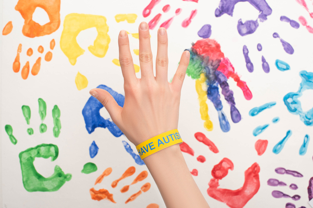 cropped view of female hand with autism bracelet on white with hand prints - Photo, Image