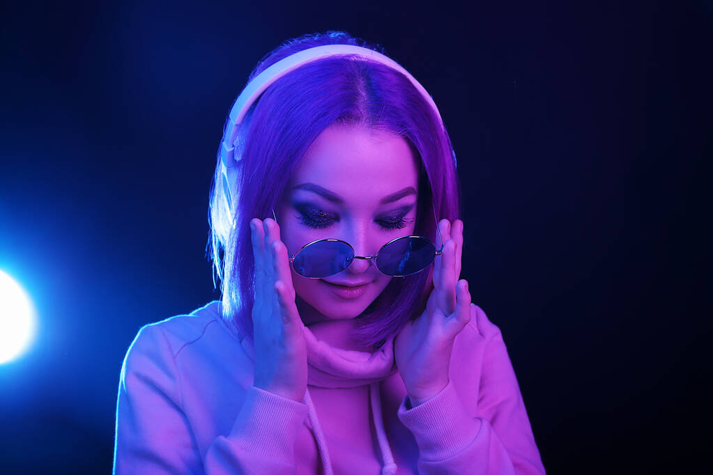 Портрет молодой женщины с фиолетовыми волосами и солнечными очками в неоновом свете и наушниках. Ночная жизнь. Поколение Y, тысячелетия
. - Фото, изображение