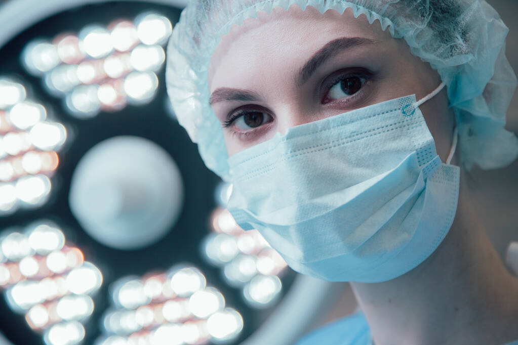 Retrato de jovem cirurgiã de uniforme médico em pé sob a lâmpada
 - Foto, Imagem
