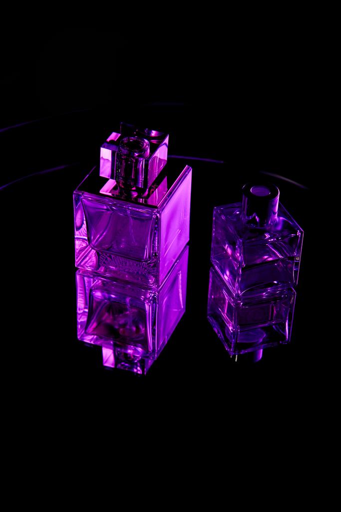 Μωβ μπουκαλάκια αρωμάτων σε καθρέφτη σκοτεινή επιφάνεια απομονωμένη σε μαύρο - Φωτογραφία, εικόνα
