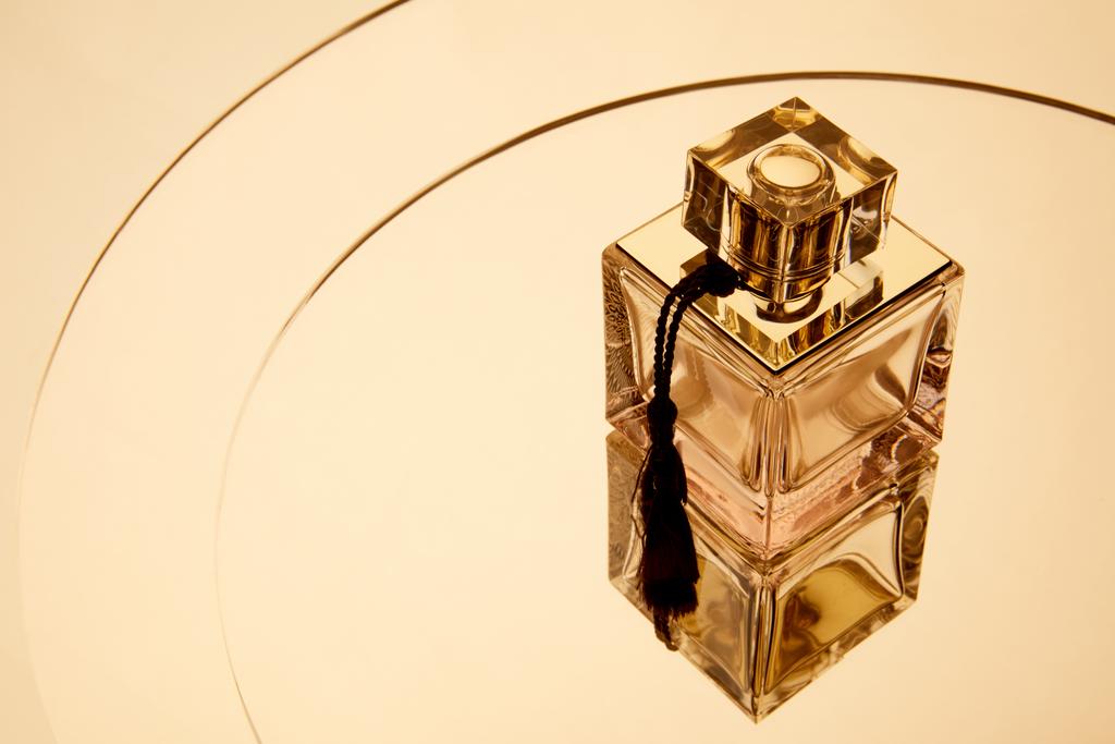 Высокий угол обзора ароматической парфюмерной бутылки на круглой зеркальной поверхности с отражением
 - Фото, изображение