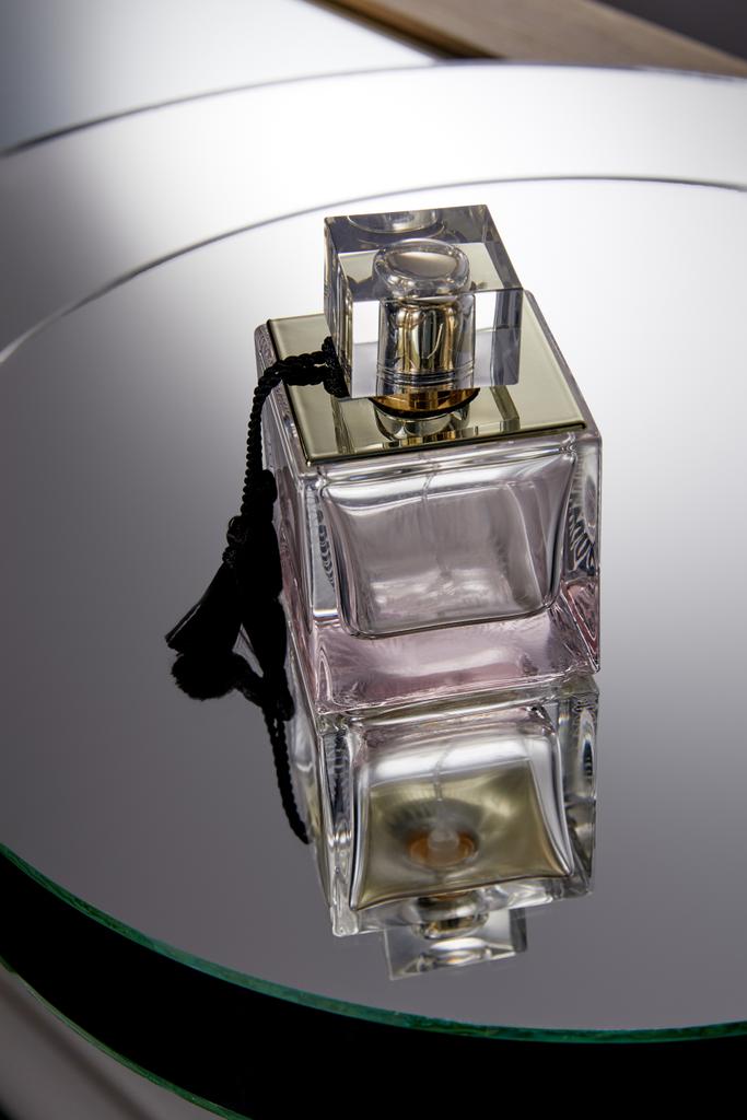 Fialová lahvička parfému na šedém kulatém zrcadlovém povrchu s odrazem - Fotografie, Obrázek