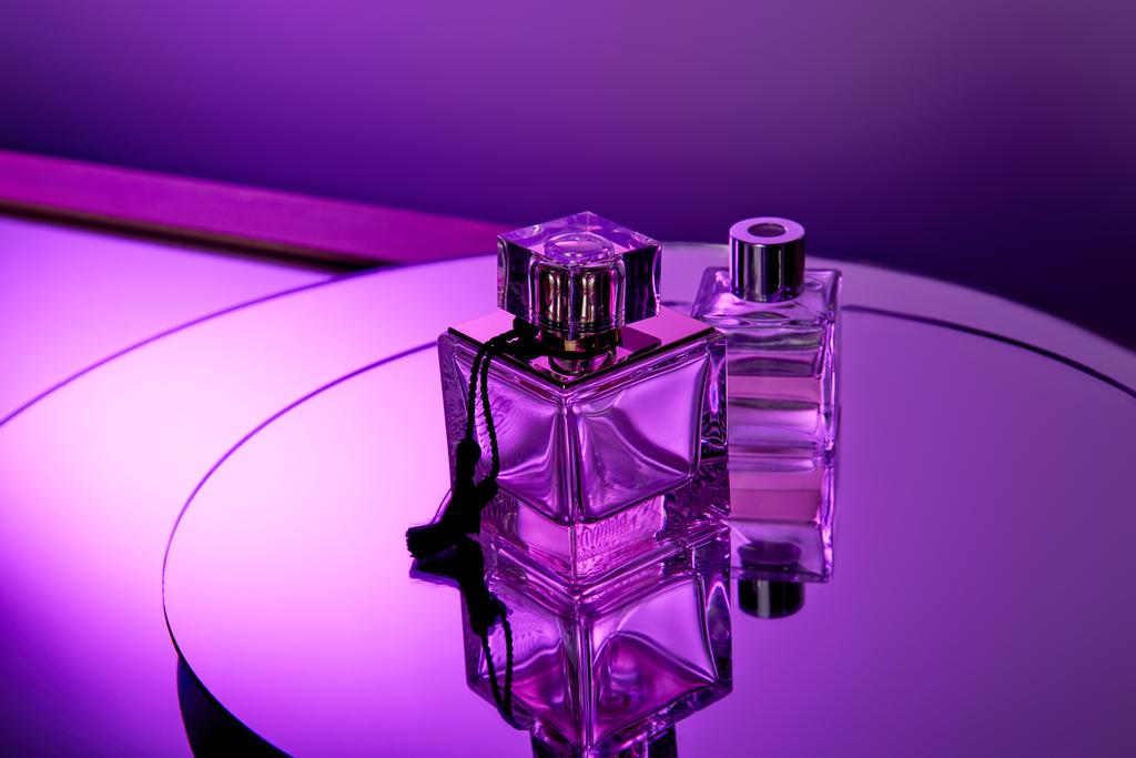 Frascos de perfume de vidrio púrpura en superficie redonda espejo violeta con reflexión
  - Foto, Imagen