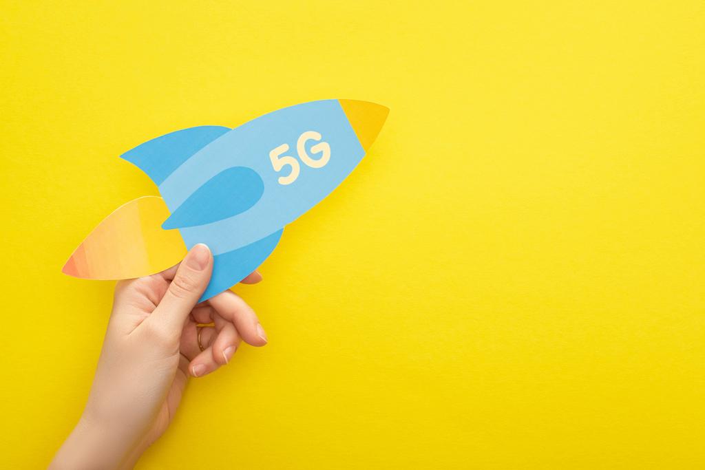 cropped view of woman holding paper rocket with 5g lettering on yellow background - Photo, Image