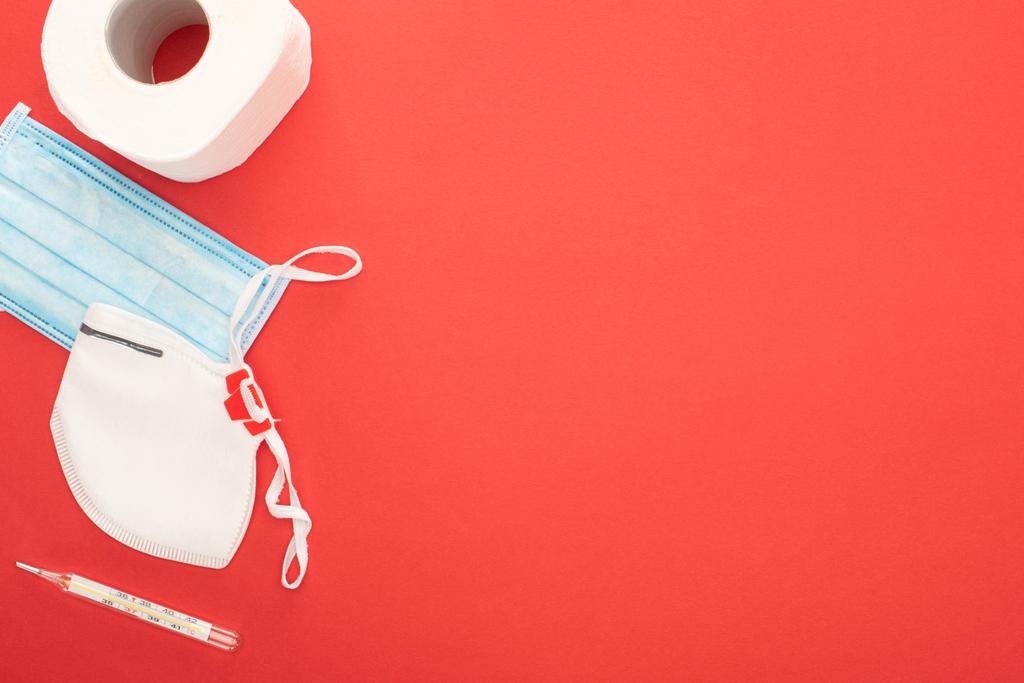 top view of white toilet paper, safety and medical masks and thermometer on red background - Photo, Image