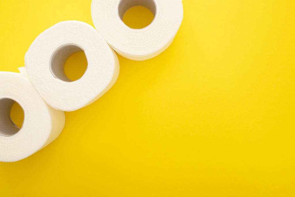Vista superior de rollos de papel higiénico blanco sobre fondo amarillo con espacio de copia - Foto, imagen