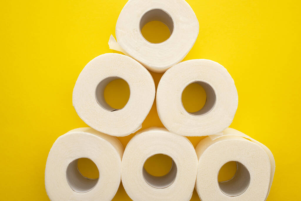 верхний вид рулонов белой туалетной бумаги, расположенных в пирамиде на желтом фоне
 - Фото, изображение