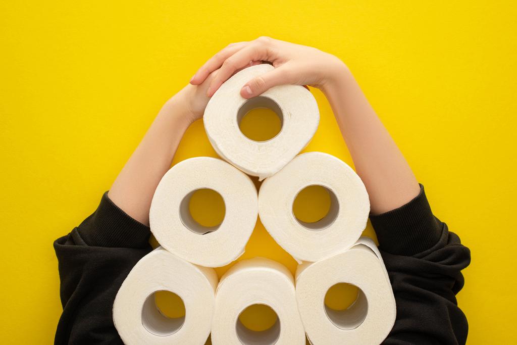 cropped view of woman grabbing white toilet paper rolls arranged in pyramid on yellow background - Photo, Image