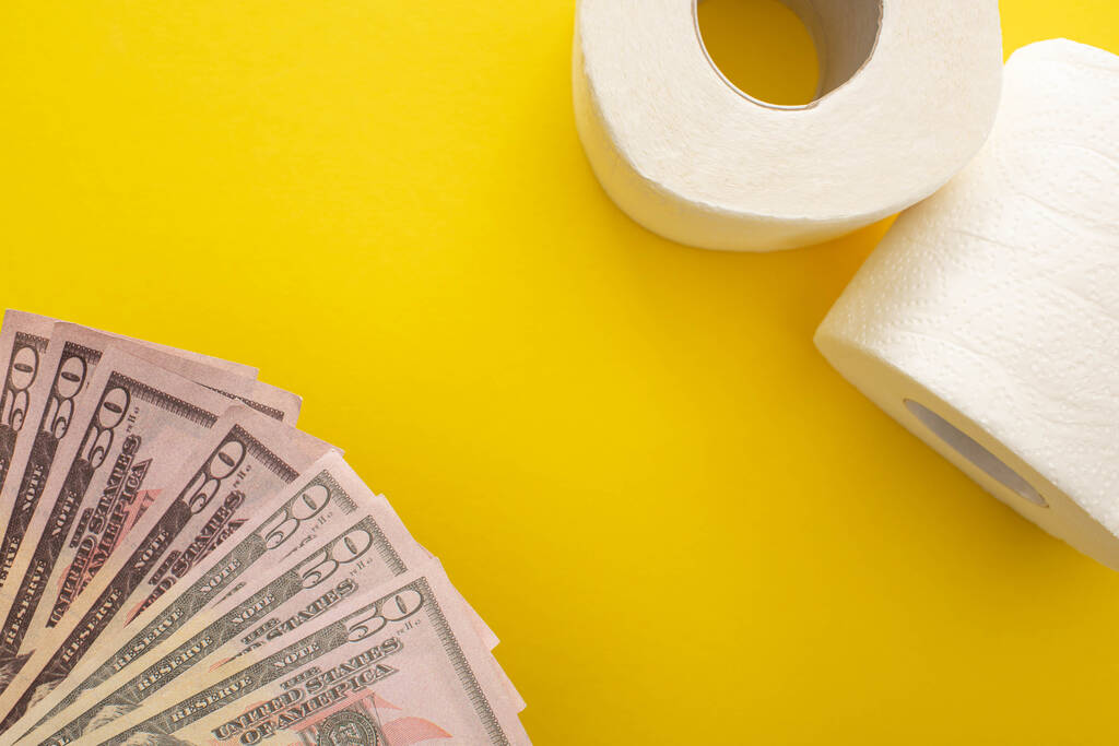 top view of white toilet paper rolls and dollars on yellow background - Photo, Image