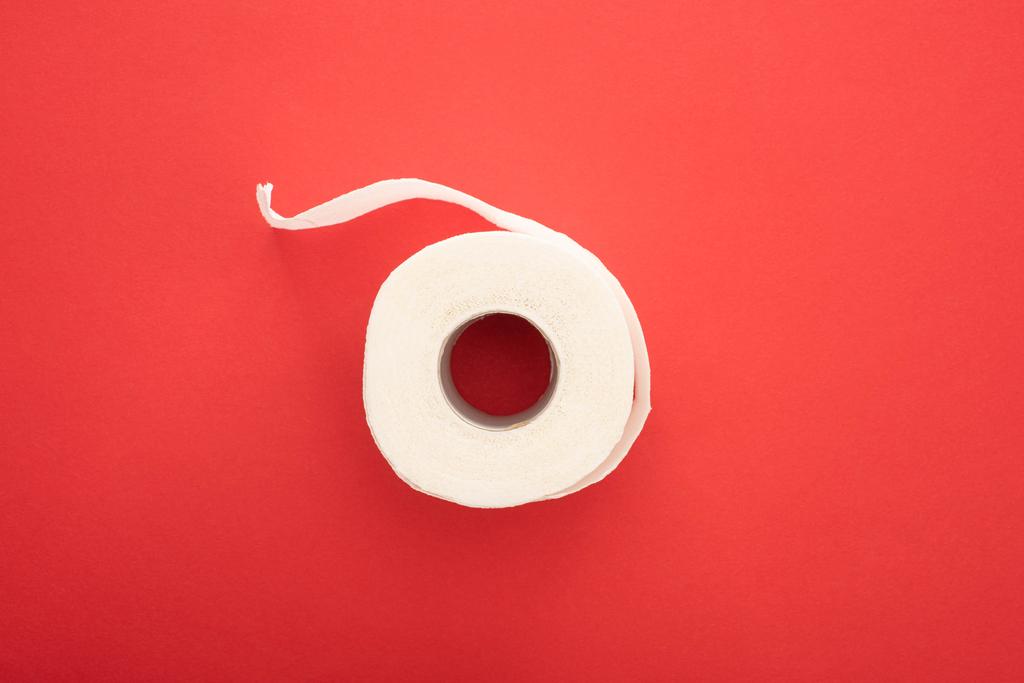 Draufsicht auf weiße Toilettenpapierrolle auf rotem Hintergrund - Foto, Bild