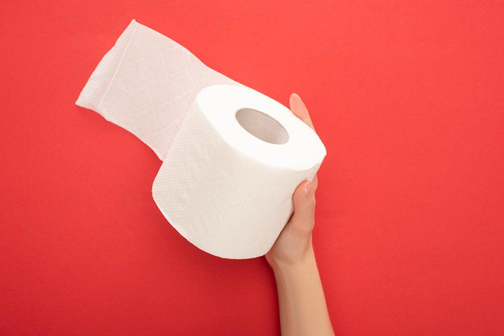 oříznutý pohled na ženu držící bílý toaletní papír role na červeném pozadí - Fotografie, Obrázek