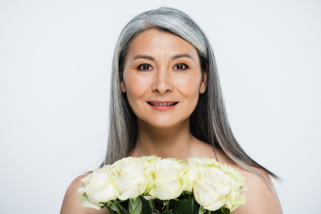 улыбающаяся голая азиатка с седыми волосами, держащая букет белых роз, изолированных на сером
 - Фото, изображение