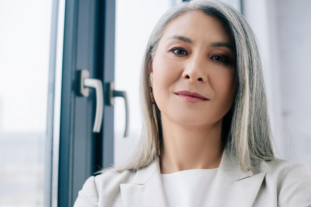 selbstbewusste asiatische Geschäftsfrau mit grauen Haaren im grauen Anzug im Büro - Foto, Bild