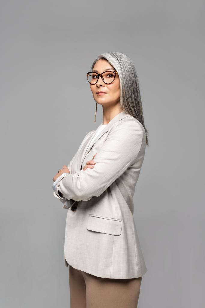 beautiful asian businesswoman in eyeglasses with crossed arms isolated on grey - Photo, Image
