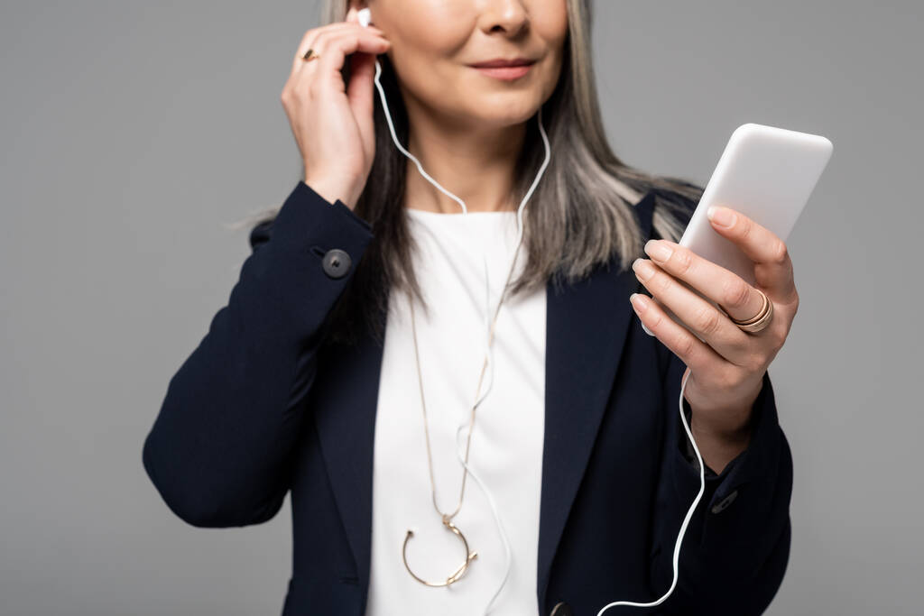 περικοπή άποψη της επιχειρηματία με γκρίζα μαλλιά ακούγοντας μουσική με ακουστικά και smartphone απομονώνονται σε γκρι - Φωτογραφία, εικόνα