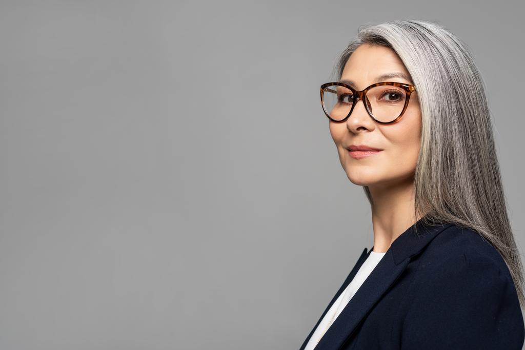 елегантна азіатська бізнес-леді з сірим волоссям в окулярах ізольована на сірому
 - Фото, зображення