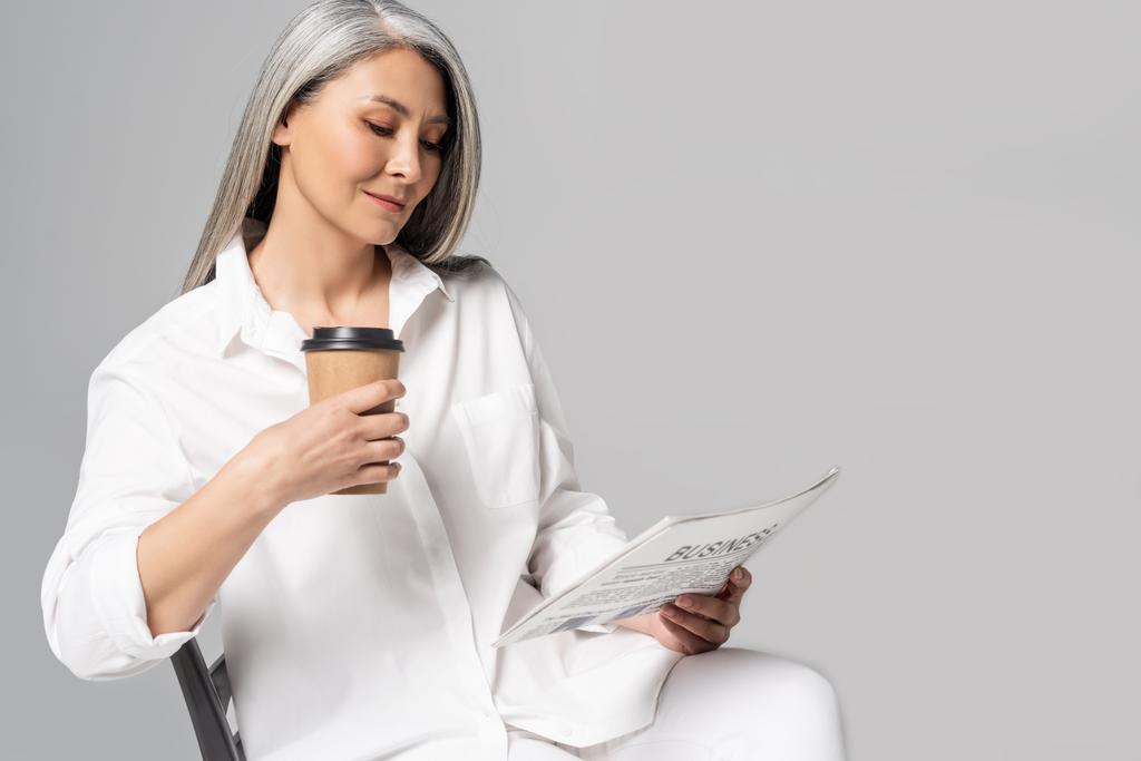 sorridente donna asiatica con i capelli grigi leggendo giornale aziendale con caffè da andare isolato su grigio
 - Foto, immagini