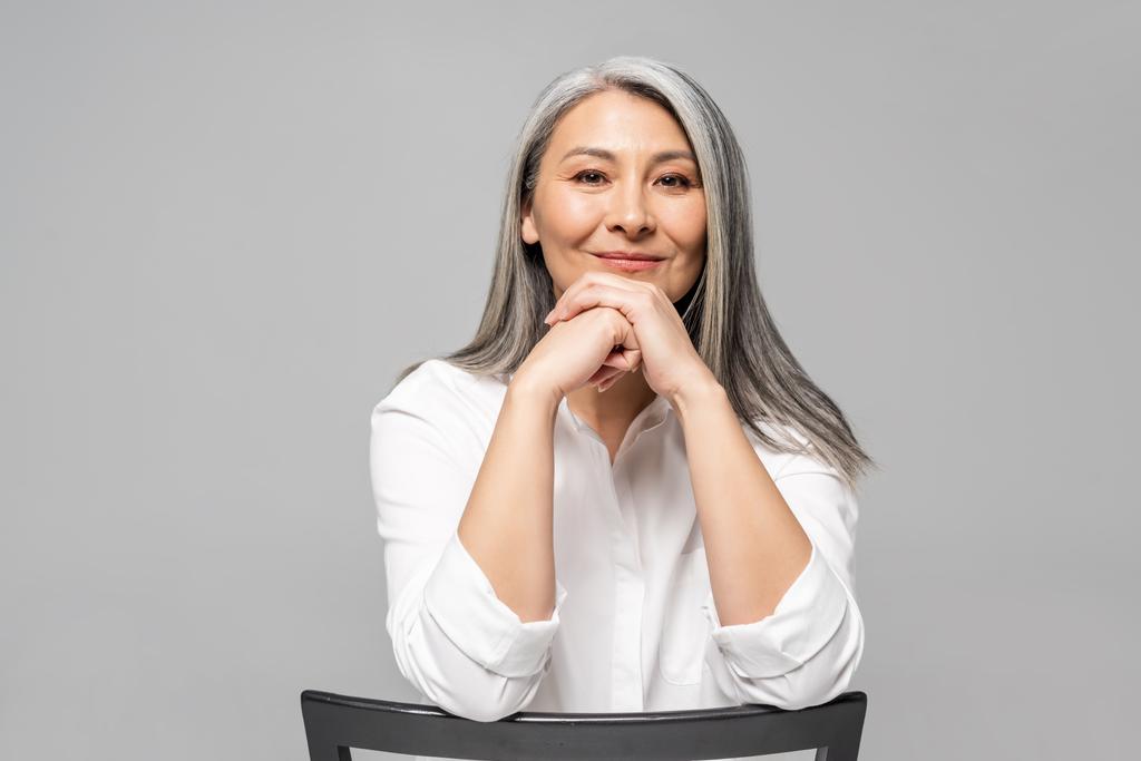 bella positivo asiatico donna con grigio capelli seduta su sedia isolato su grigio
 - Foto, immagini