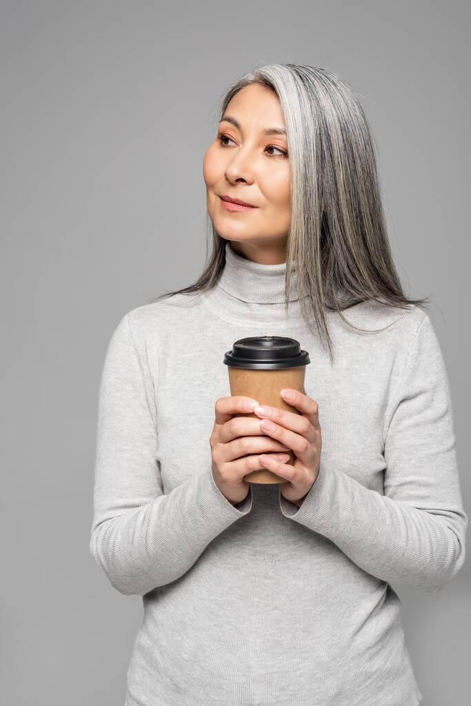 灰色の髪をしたアジア系女性がコーヒーを持ってグレーで隔離され - 写真・画像