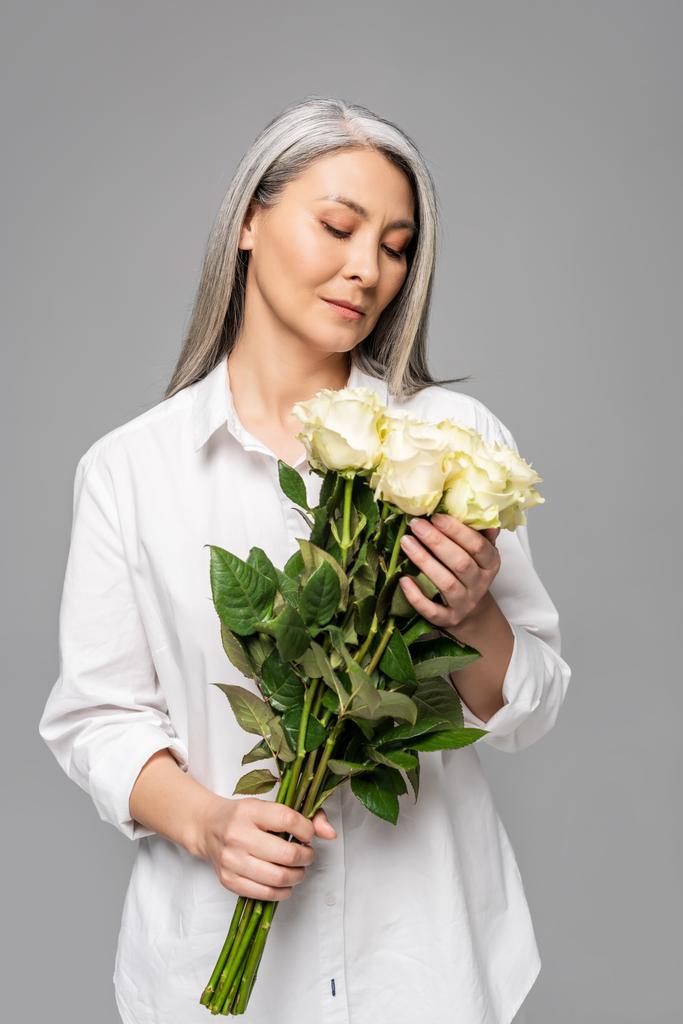 Erwachsene asiatische Frau mit grauen Haaren hält Strauß weißer Rosen isoliert auf grau - Foto, Bild