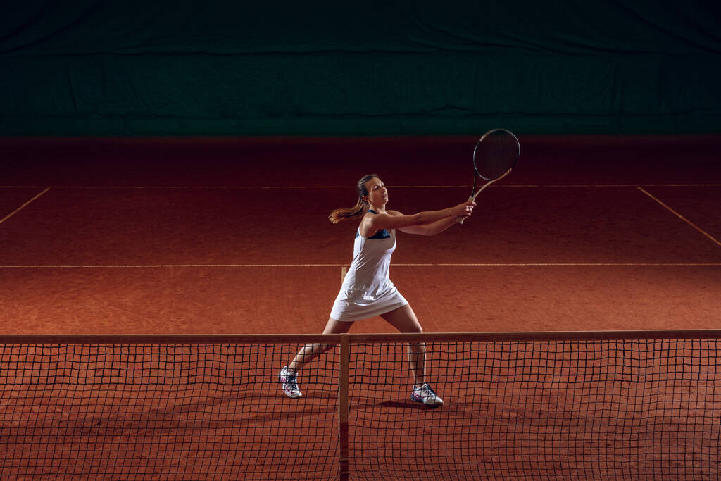 若い白人プロのスポーツ女性がスポーツコートの背景でテニスをする - 写真・画像