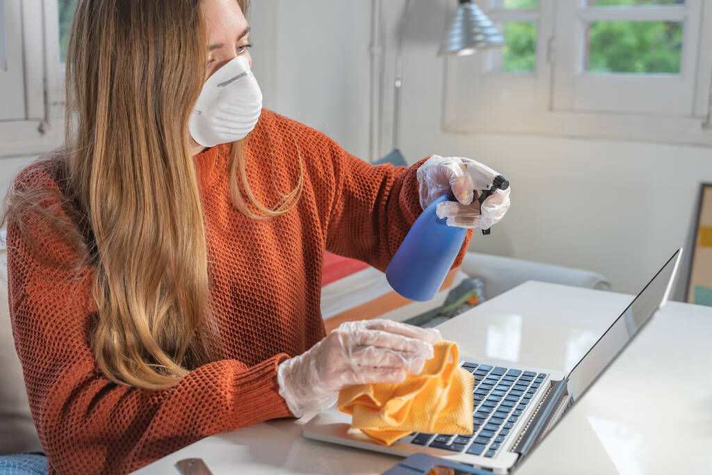 Coronavirus. Woman with face mask and rubber gloves cleaning stuff with a disinfectant at home during the coronavirus epidemic. Infection prevention and control of epidemic. Disinfect your house. - Photo, Image