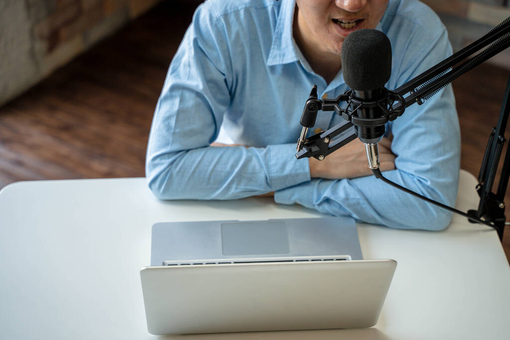 Young adult businessman podcasting and recording talk show at home studio with computer laptop on table. The desk is attached with microphone. - Photo, Image