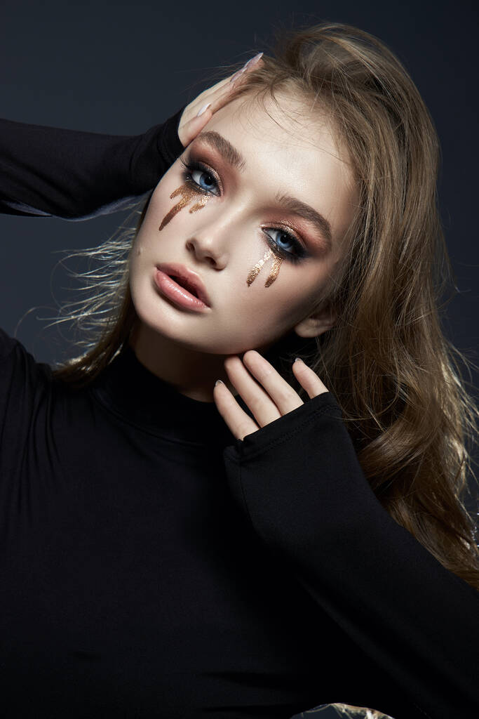 Beauty portrait blonde woman with makeup and big blue eyes, natural cosmetics, clean delicate skin of the girl face, black clothes. Drops of makeup trickle from the girl eyes - Photo, Image