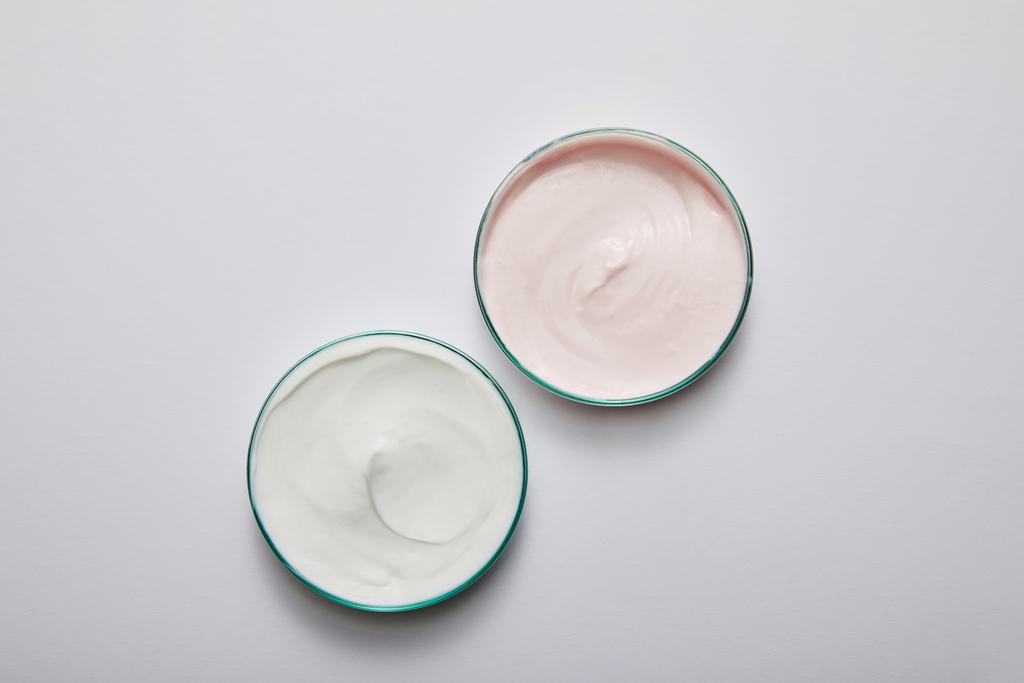 A fehér és rózsaszín kozmetikai krémmel ellátott laboratóriumi üvegáruk felülnézete szürke alapon - Fotó, kép