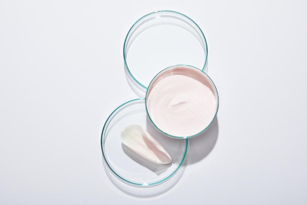 Top kilátás laboratóriumi üvegáru rózsaszín kozmetikai krém és rózsaszirom szürke háttér - Fotó, kép