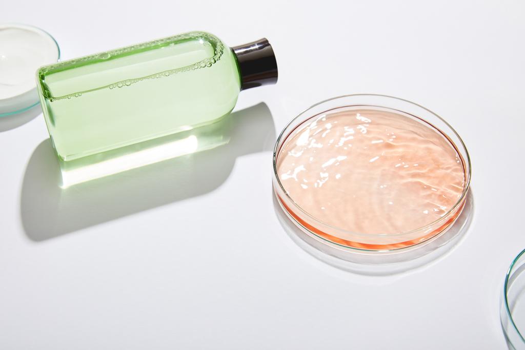 Butelka kosmetyczna z zielonym płynem i laboratoryjnym szkłem z płynem i kremem kosmetycznym na szarym tle  - Zdjęcie, obraz
