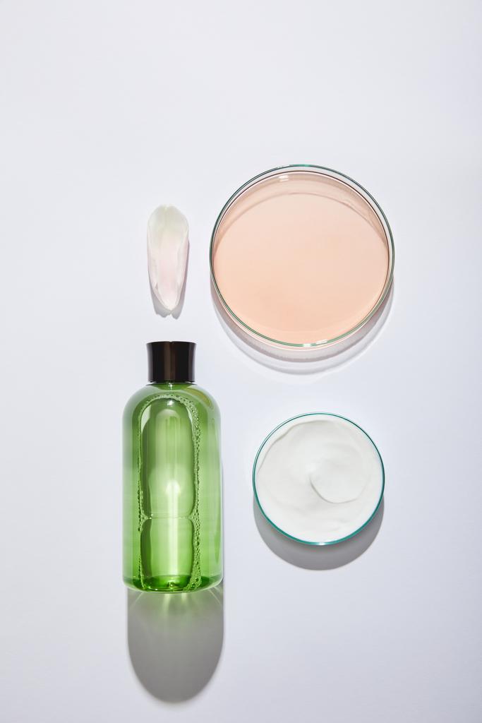 Yeşil sıvılı kozmetik şişesi, beyaz kozmetik kremli kavanoz ve gri arka planda sıvı bulunan laboratuvar camlarıyla düz yatıyordu.  - Fotoğraf, Görsel