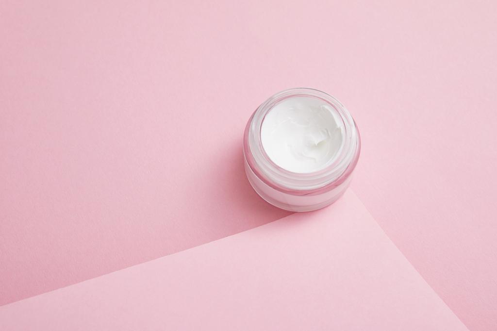 Cosmetische crème in glazen pot op roze achtergrond  - Foto, afbeelding