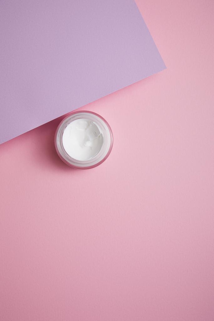 Draufsicht auf kosmetische Creme im Glas auf rosa und lila Hintergrund  - Foto, Bild
